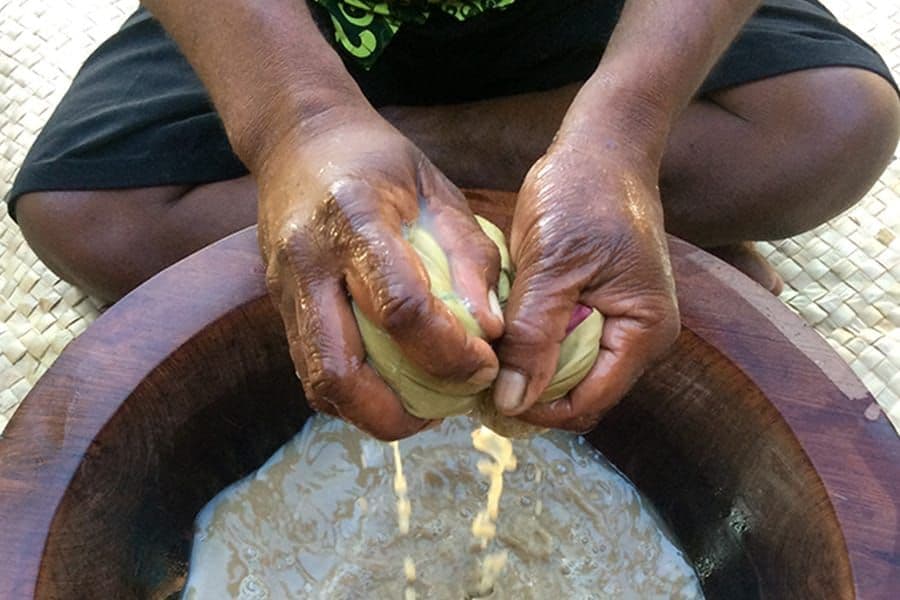 Hands squeezing kava root over a wooden bowl during a traditional kava ceremony in Vanuatu
