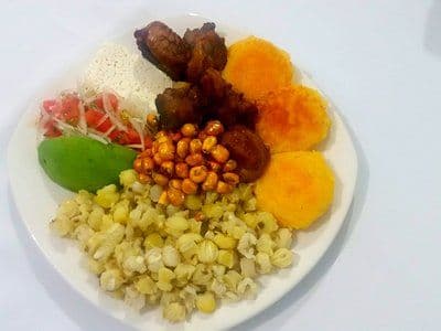 A white plate holding a traditional Ecuadorian highland meal with rice, fried meat, corn, and vegetables, typical of Atuntaqui dining.