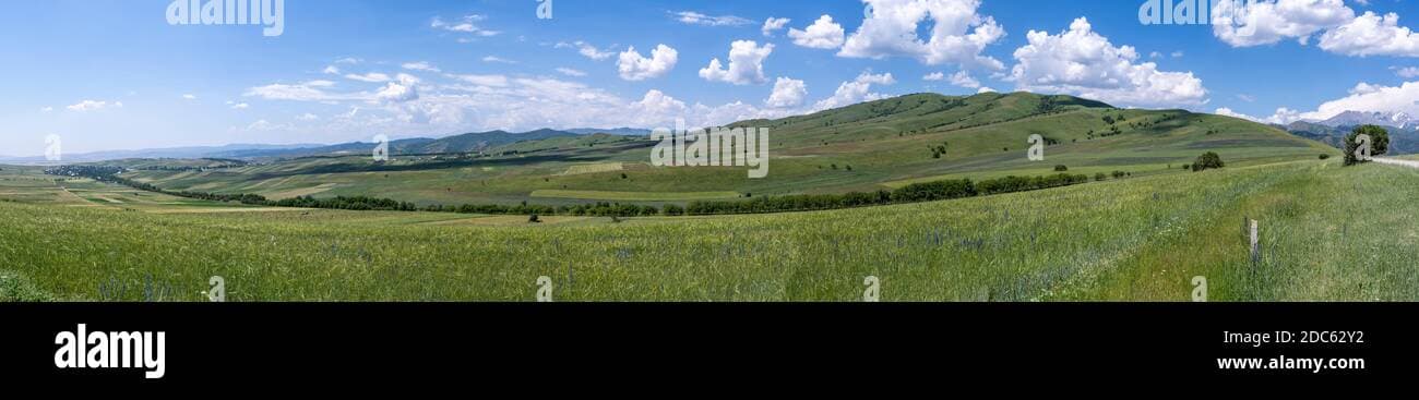 Wide landscape of terraced green hills and fields in the Suzak district of the Fergana Valley, Kyrgyzstan