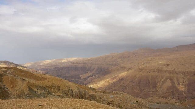 Wide dry highland landscape near Al Khinzīrah, Jordan, with rolling brown terrain, eroded slopes, and a cloudy sky.