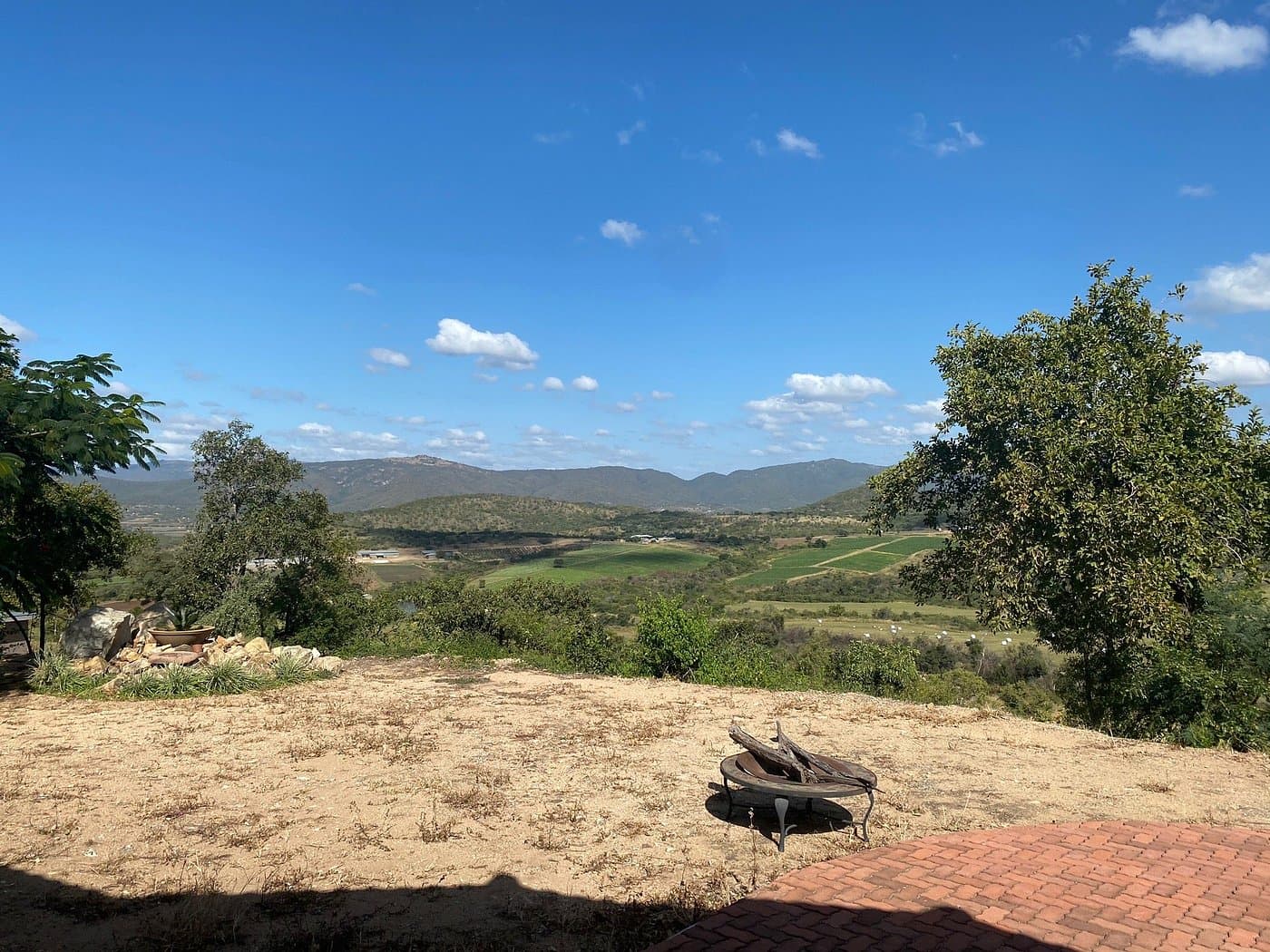 A scenic landscape view of the Sidvokodvo area featuring rolling green hills, distant mountains, and a clear blue sky with scattered clouds.