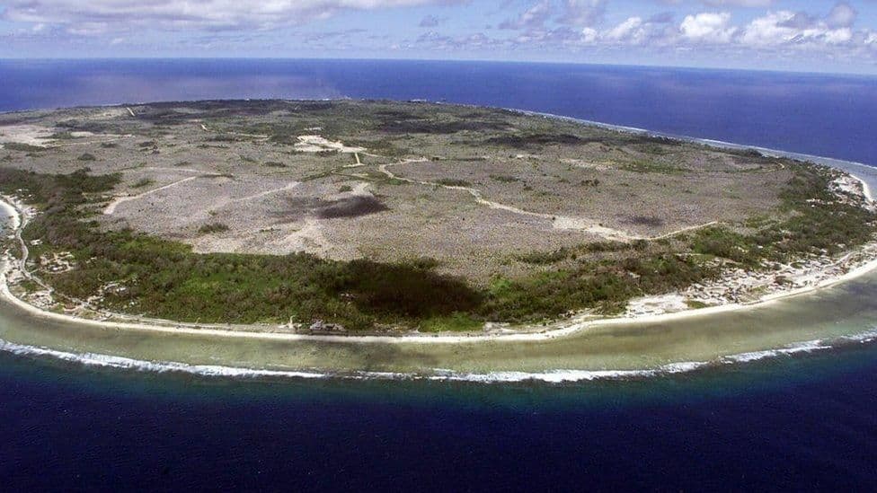 Aerial view of Nauru's small island terrain, showing sparse vegetation, cleared land, and surrounding coastline.