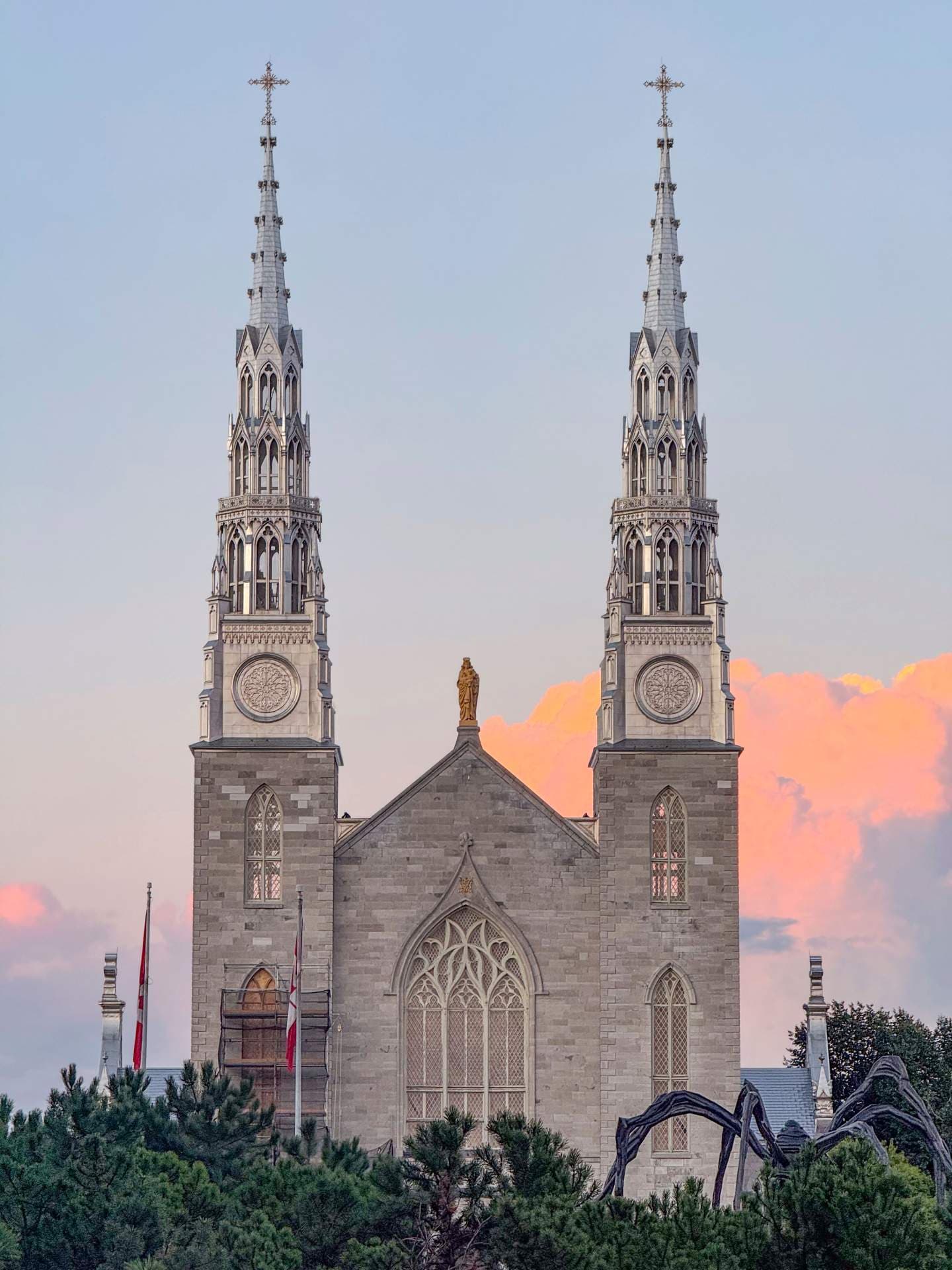 Exterior of a Gothic Revival church with twin spires, stone facade, arched windows, and a sunset sky.