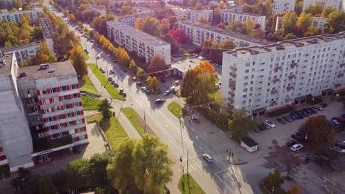 Aerial view of a residential streetscape with multi-story apartment buildings, autumn trees, and a wide road with light traffic.