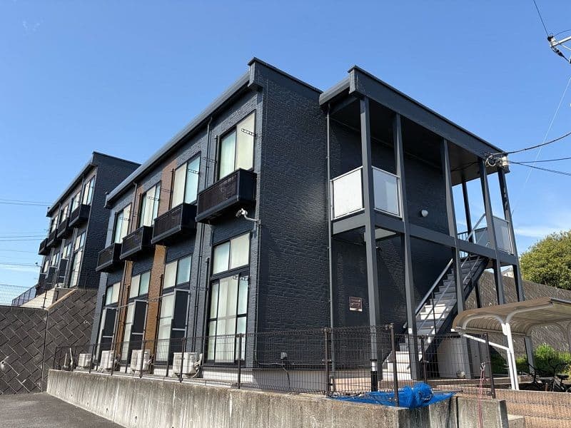 Exterior view of a modern black brick building with balconies and external stairs under a clear blue sky