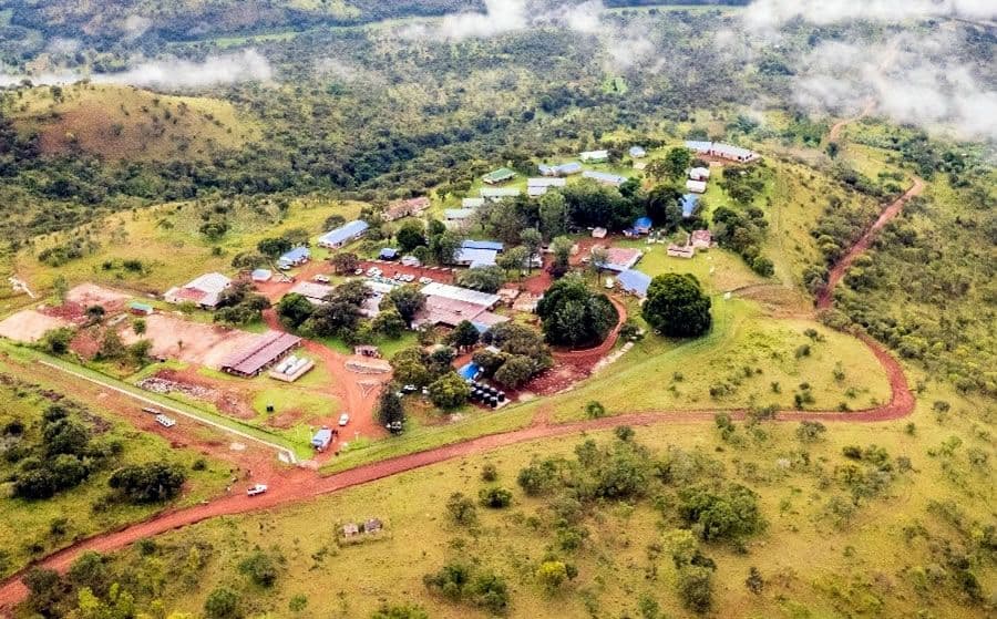 Aerial view of a rural settlement with scattered buildings, dirt roads, and green hills in a misty landscape in the Kagera region.