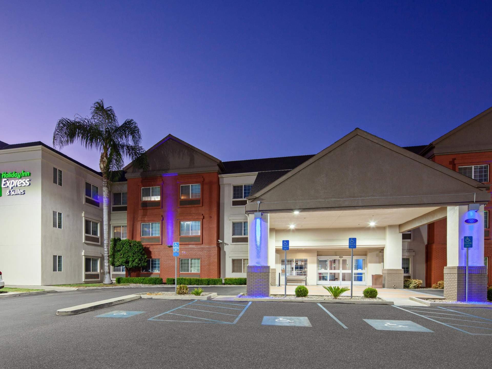Exterior of a Holiday Inn Express hotel at dusk, with parking lot, palm tree, and illuminated entrance.