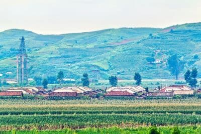 Wide landscape photograph of green farmland and rolling hills with a small village and a tall tower in the distance.