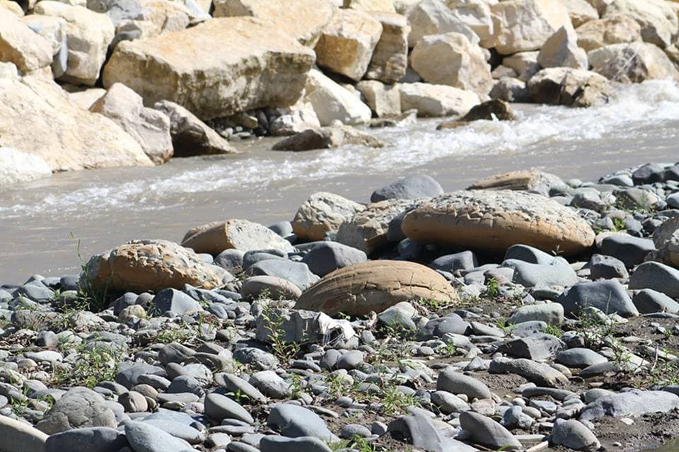 A rocky riverbank with smooth stones and flowing water, depicting the natural scenery along the Khanistskali river in Baghdati.