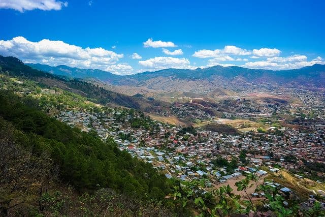 Aerial view of a hillside town nestled in a mountain valley under a blue sky with scattered clouds.