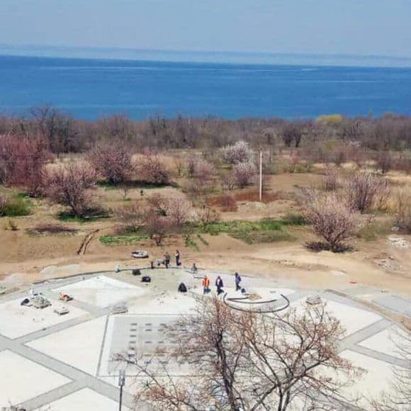 Aerial view of a paved plaza and park in Dniprorudne with a large body of water in the background, showing the town's layout near the Kachovka Reservoir.