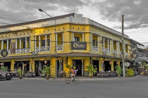 A yellow two-story building with a balcony stands on a street corner in Thakhèk, with a cyclist passing by in the foreground.