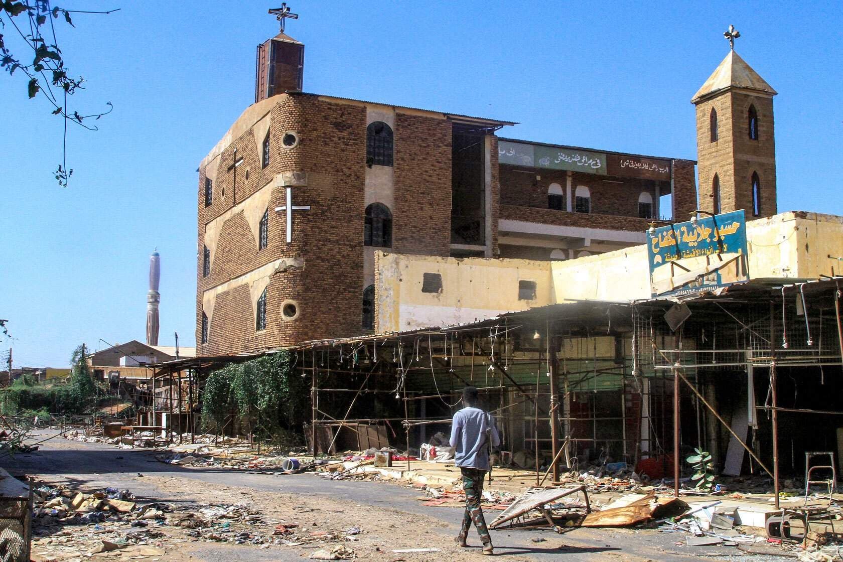 Exterior of a brick church with crosses and a minaret in a South Sudan town, with a man walking past.