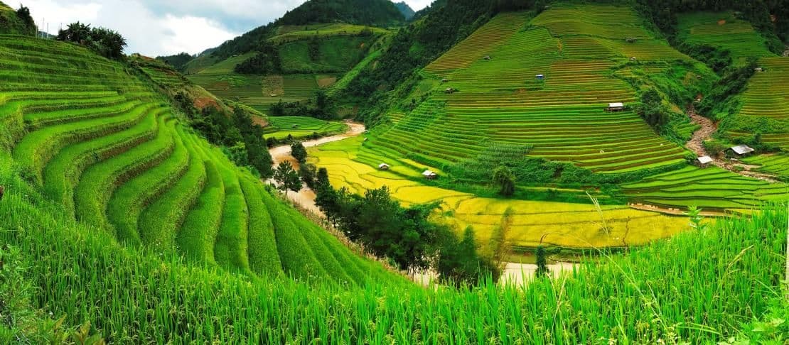 Terraced green hillsides with a winding river and scattered huts in a mountainous landscape near Chuka, Kenya.