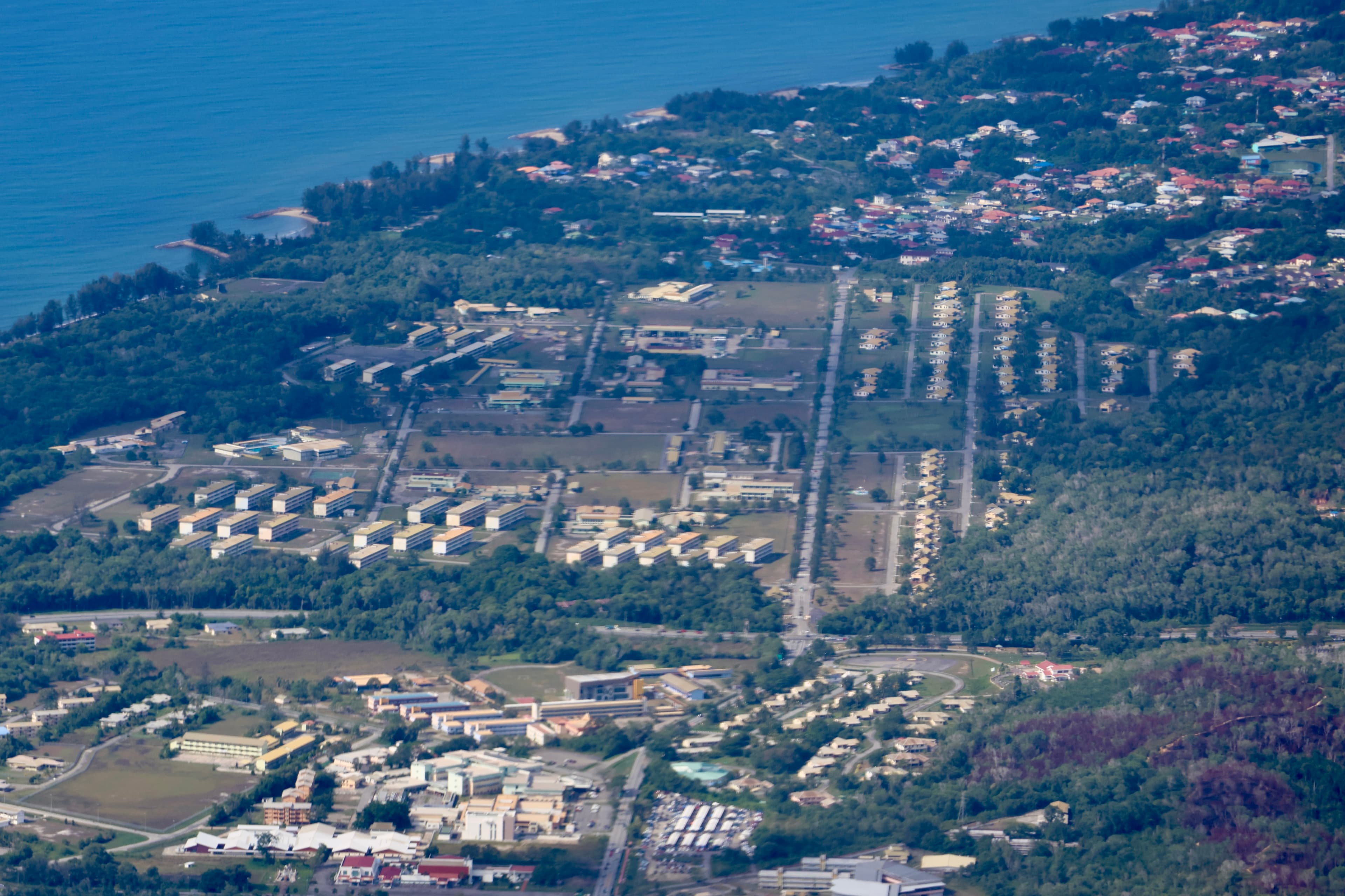 Aerial view of Tutong district showing coastal development, organized housing blocks, and dense greenery along the Brunei shoreline.