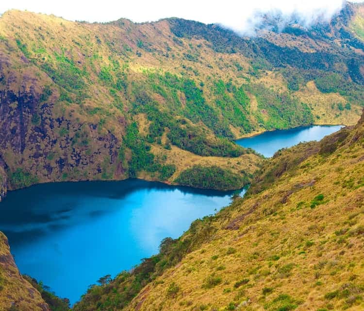 Aerial view of twin blue crater lakes nestled within steep, grassy volcanic slopes, characteristic of Mount Wilhelm's landscape near Kundiawa.