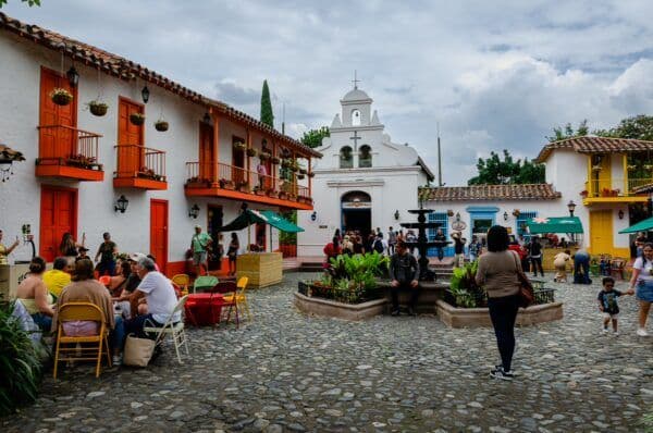 Cobblestone plaza in a small Honduran town with colorful colonial buildings, a white church, and people dining and walking.