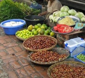Open-air market display with baskets of beans, bowls of fruit, and vegetables on a brick floor in a West African market.