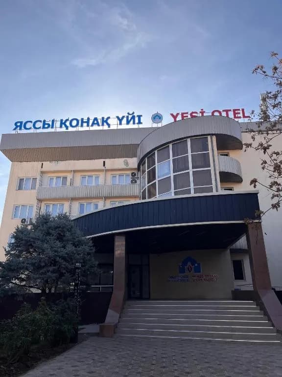 Exterior of a multi-story hotel building with Kazakh and Turkish signage, entrance steps, and clear sky.