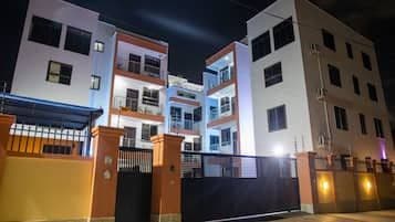 Nighttime exterior of multi-story residential buildings with illuminated windows and a gated entrance in the Anloga town center.