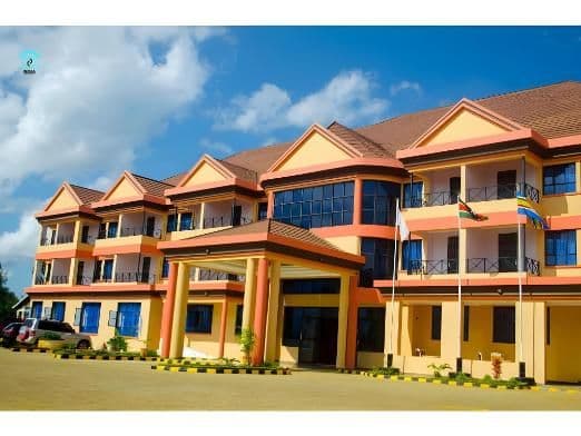Exterior of a multi-story building in Chuka, Kenya, with an orange and yellow facade, tiled roof, and flags under a blue sky.