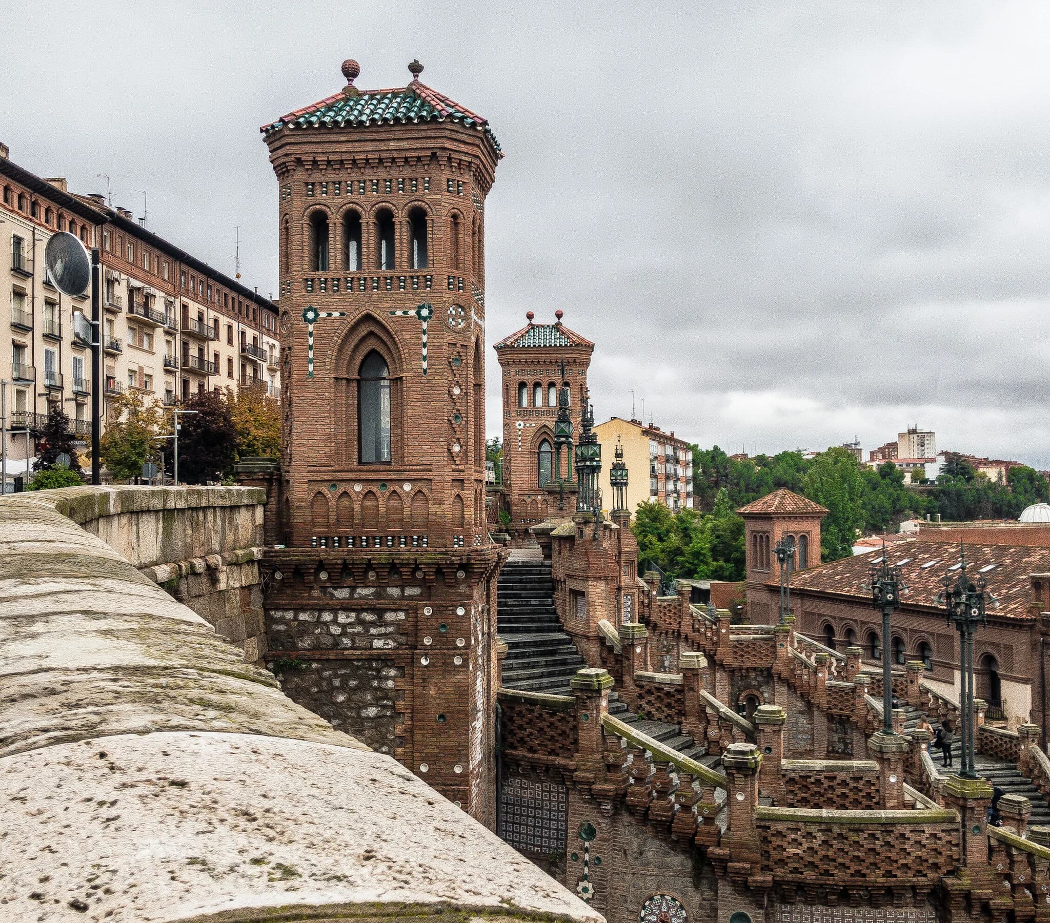 Detailed view of the ornate brick towers and staircases of the San Pedro Cathedral in Teruel, Spain, set against an overcast sky.
