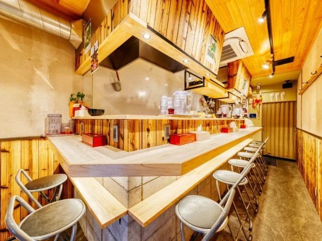 Interior view of a small restaurant with a long wooden counter, metal stools, and wood-paneled walls