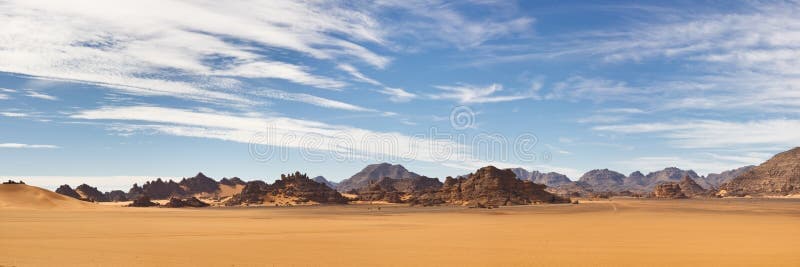 Wide-angle desert landscape at dawn in the Akakus region of Libya, showcasing rock formations and vast open terrain