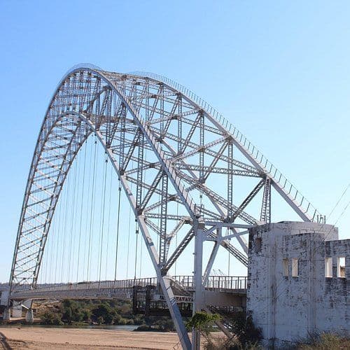 Large steel arch bridge with concrete abutment under clear blue sky in the Chipinge area.