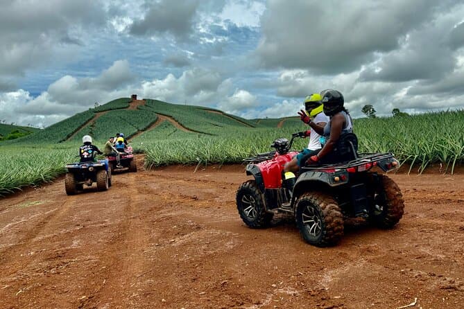 Red dirt road winding through rural sugarcane fields under a cloudy sky