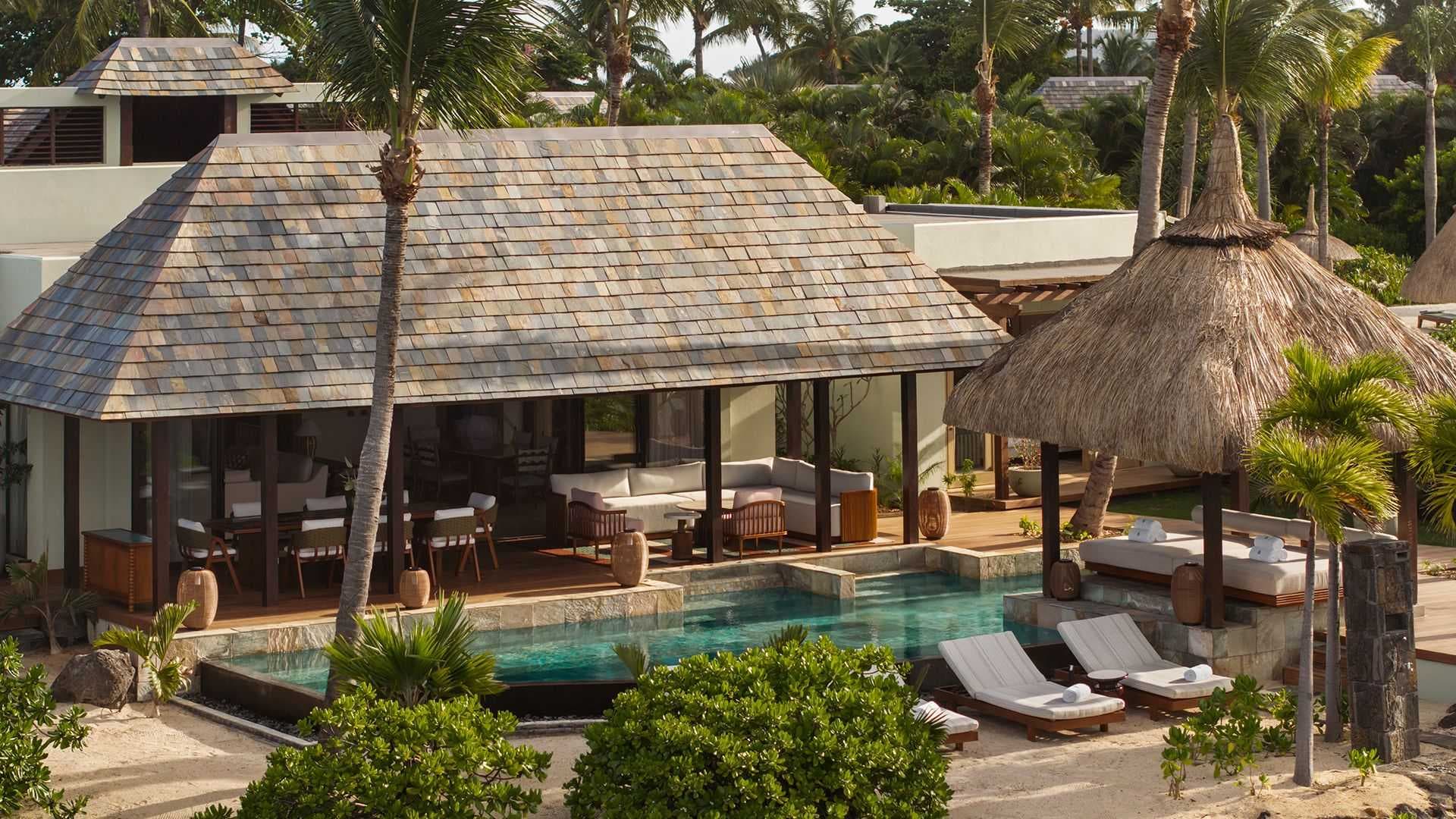 Luxury tropical resort villa exterior with shingled roof, private pool, lounge chairs, and palm trees.