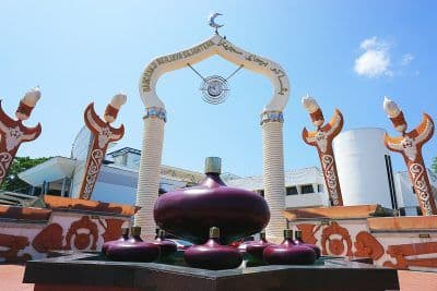 Low-angle exterior shot of the Keris Monument in Tutong, featuring a large purple keris sculpture beneath an ornate archway against a blue sky.