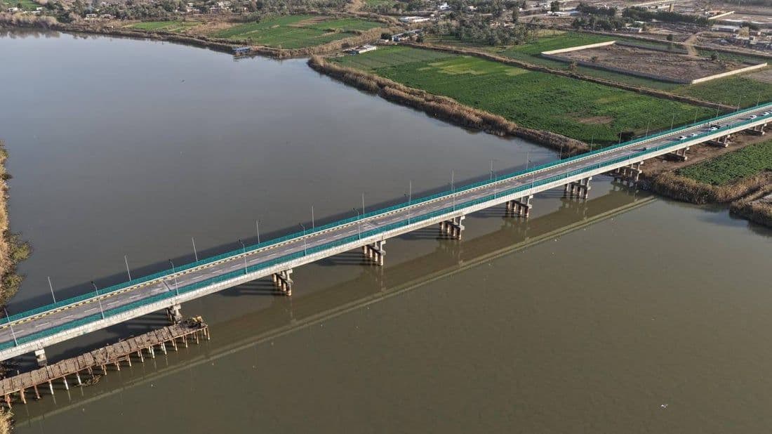 Long concrete bridge crossing the Tigris River in Kut, Iraq, with green fields and rural settlements nearby.