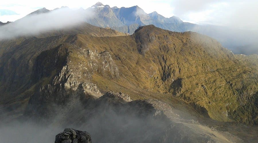 Misty mountain landscape featuring steep, rugged highland terrain with rocky ridges and distant peaks, characteristic of the Mount Wilhelm region.