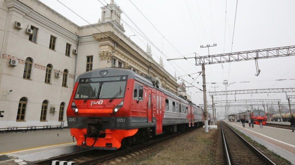 Red and grey RZD electric train at a historic white railway station platform under overcast skies.