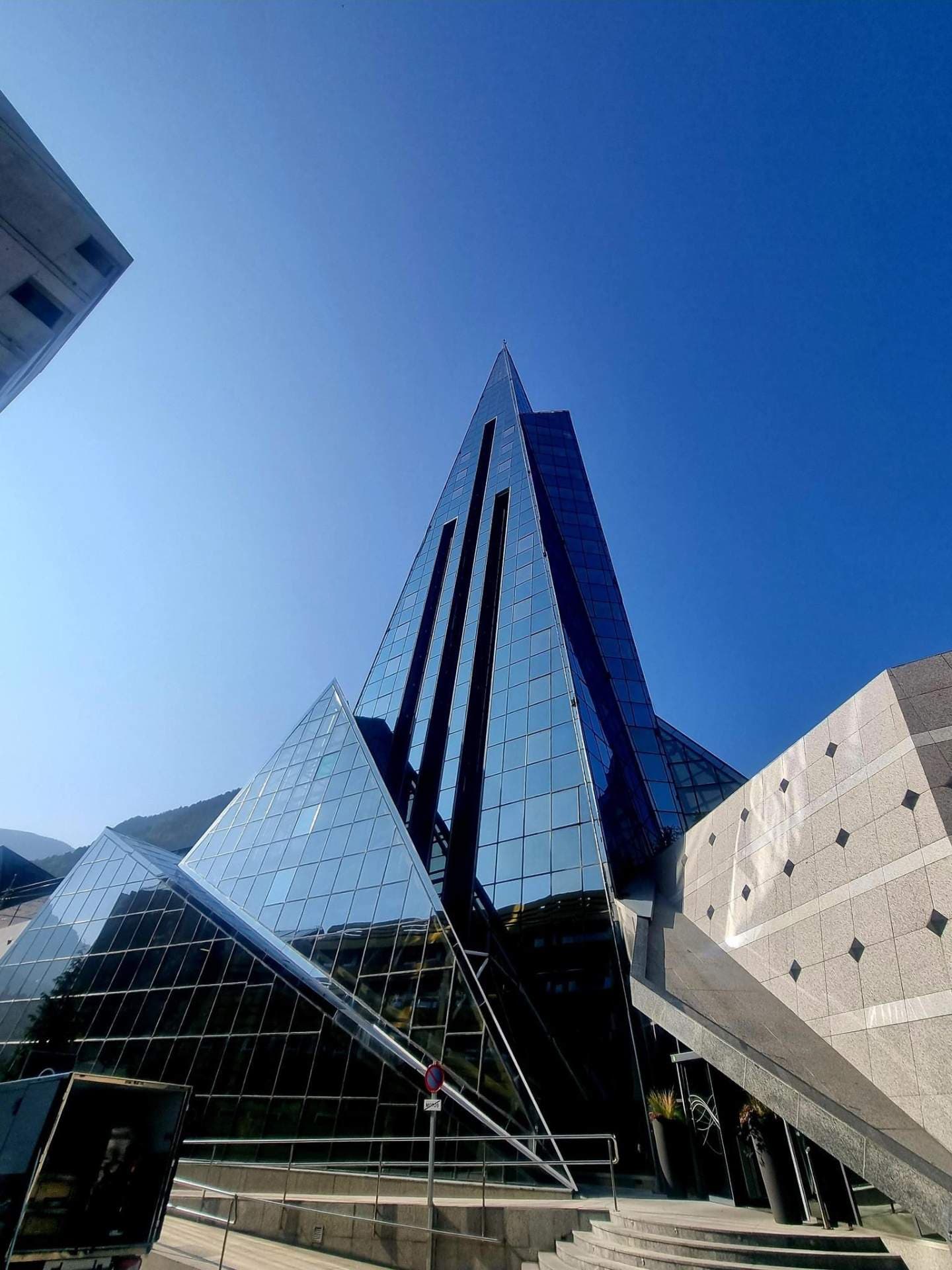 Low-angle exterior of the angular glass Caldea thermal spa building against a clear blue sky.