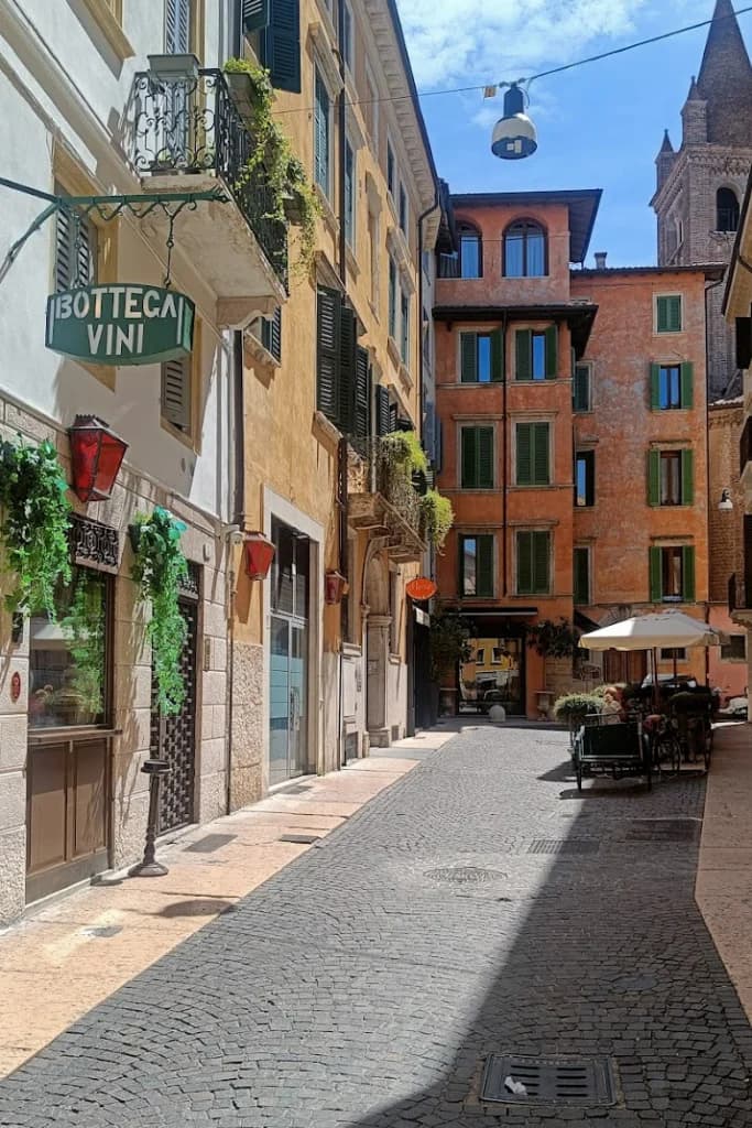 Sunlit cobblestone street in Veneto featuring a wine shop sign, historic architecture, and outdoor seating.