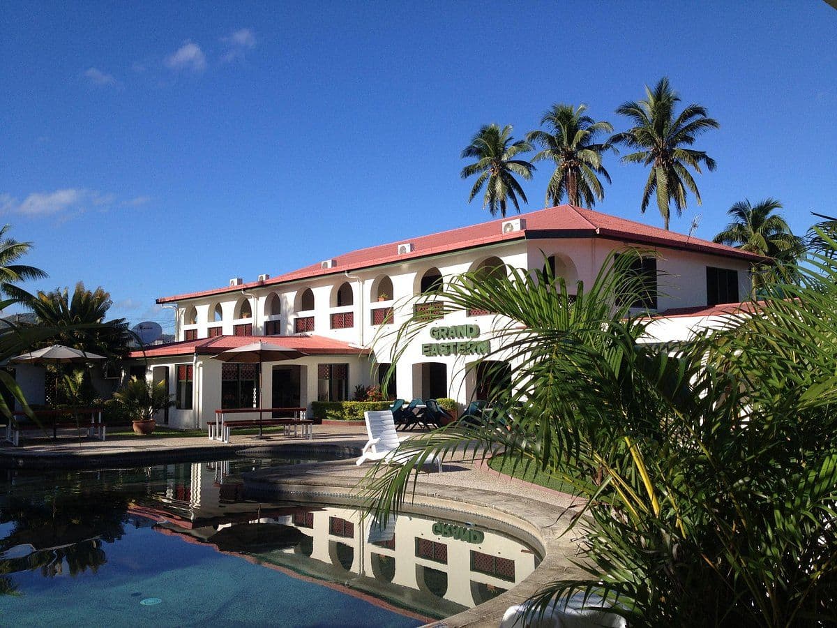 Exterior view of the Grand Eastern hotel in Labasa, featuring a white building with a red roof, palm trees, and a swimming pool.