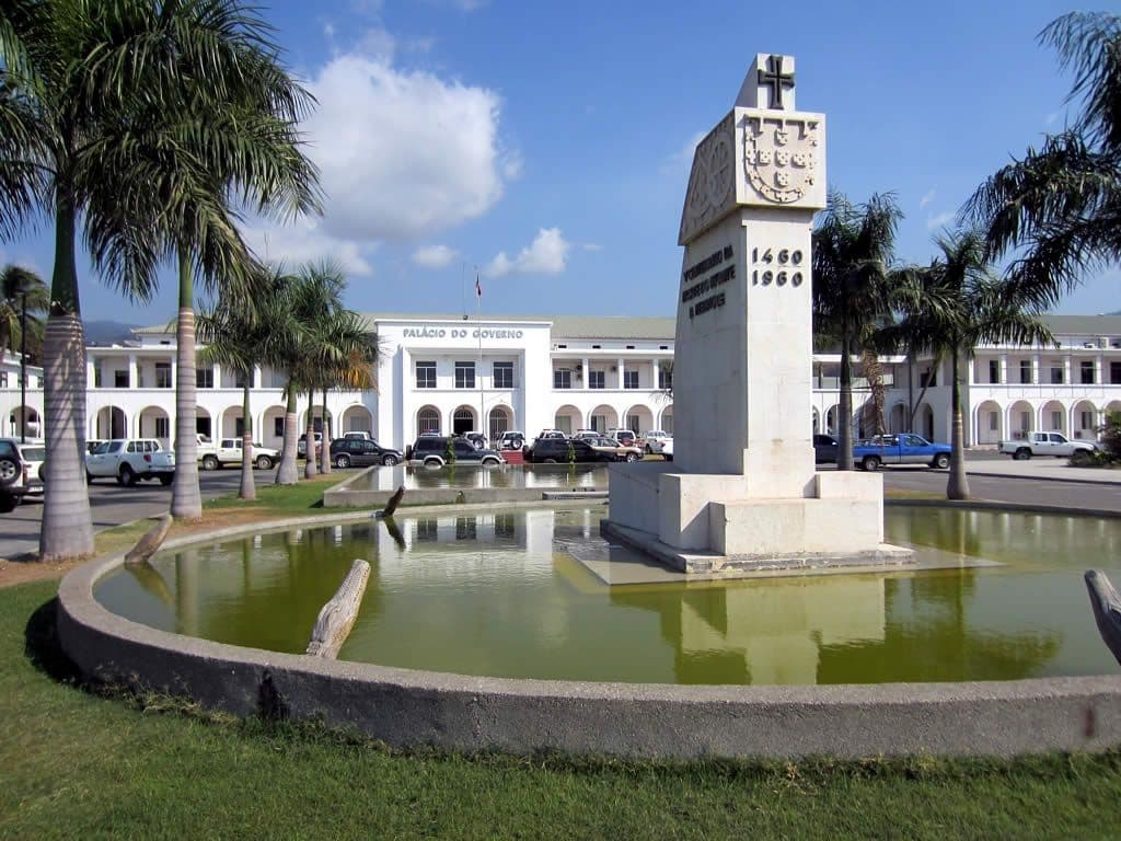 Government palace exterior with a commemorative monument and fountain in a palm-lined plaza