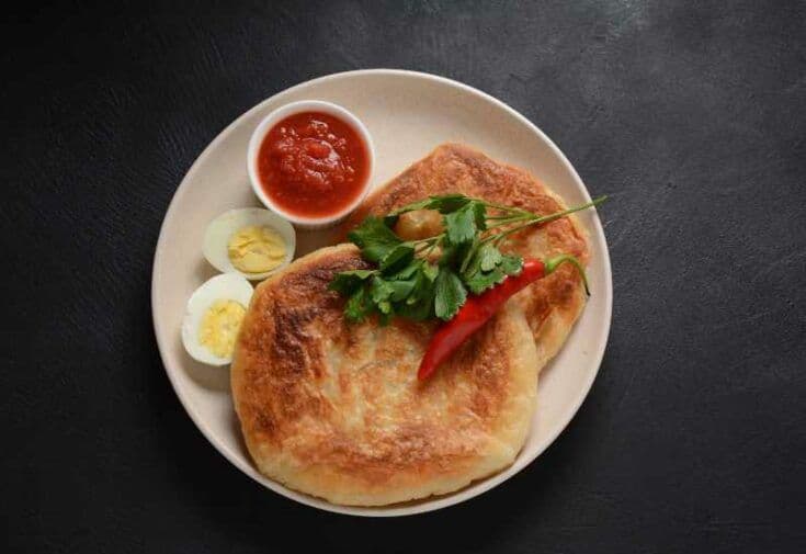 Overhead shot of golden-brown malawach flatbread served on a plate with hard-boiled eggs, chili, and sauce.