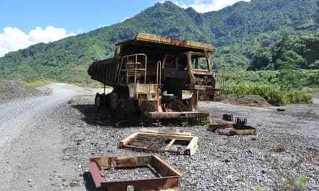 Rusted dump truck on a gravel road in a mountainous, forested landscape