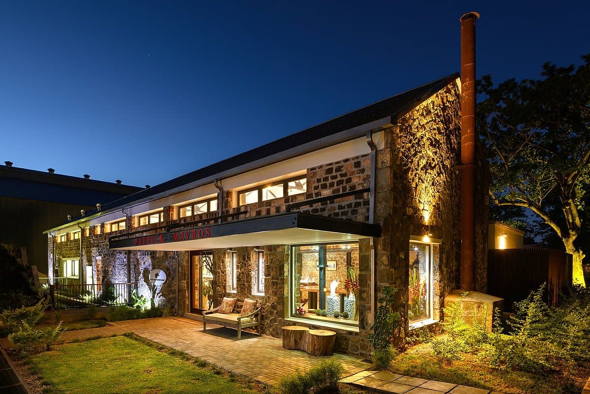 Night exterior of the Patrick Mavros jewelry atelier in Terre Rouge, featuring stone architecture, warm lighting, and a visible sign.
