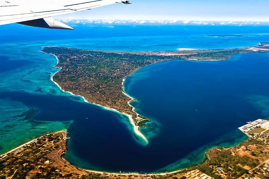 Aerial coastal view of a tropical island with turquoise waters, sandy beaches, and green vegetation, seen from an airplane window over Mtwara, southern Tanzania