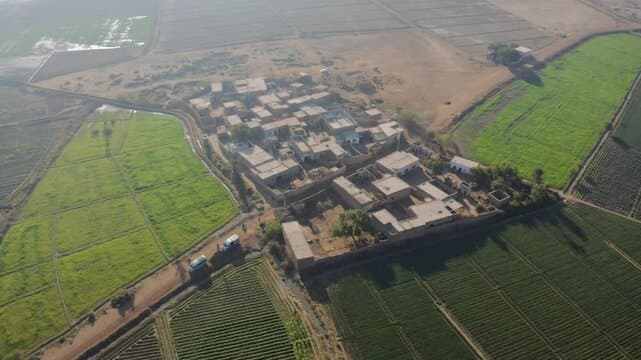 Aerial view of a rural village in Sindh, Pakistan, surrounded by vibrant green agricultural fields and arid land.