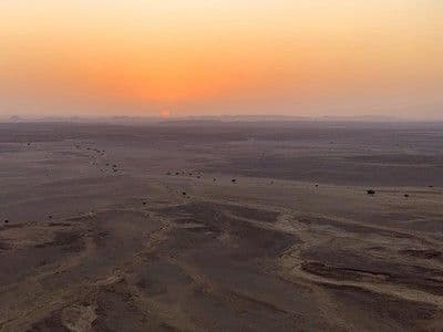 Aerial view of a vast, flat desert plain at sunset with a hazy orange sky and distant horizon in central Iraq.