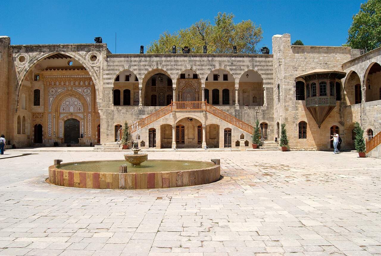 Stone courtyard of Beiteddine Palace in the Chouf Mountains, featuring arched galleries and a central fountain under a clear blue sky.