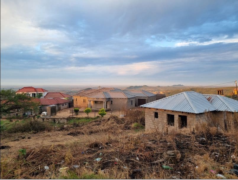 Rural village with brick and corrugated metal-roofed houses on a hillside, dry grass, and distant hills in Eswatini