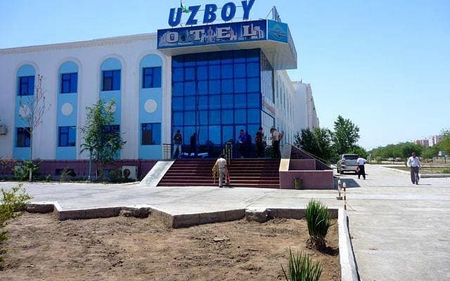 Exterior view of the Uzboy Hotel in Dashoguz, featuring a white facade with blue accents, a glass entrance, and guests on the steps.