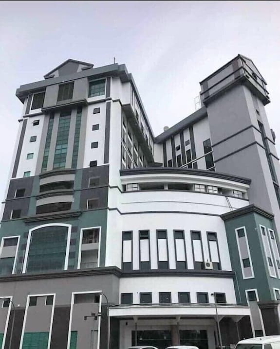 Low-angle exterior view of a modern multi-story building featuring white, grey, and green architectural elements under an overcast sky.