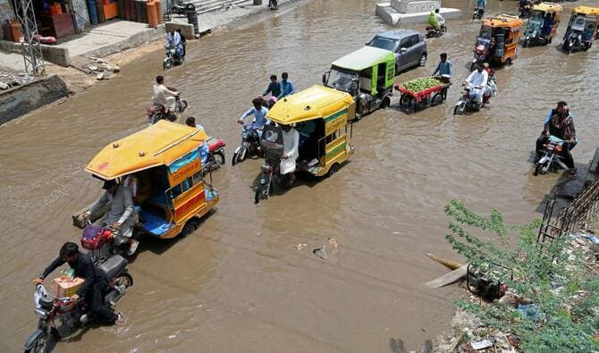 Auto-rickshaws and motorcycles navigate a flooded street in Sindh, Pakistan, capturing local transportation amidst urban waterlogging.
